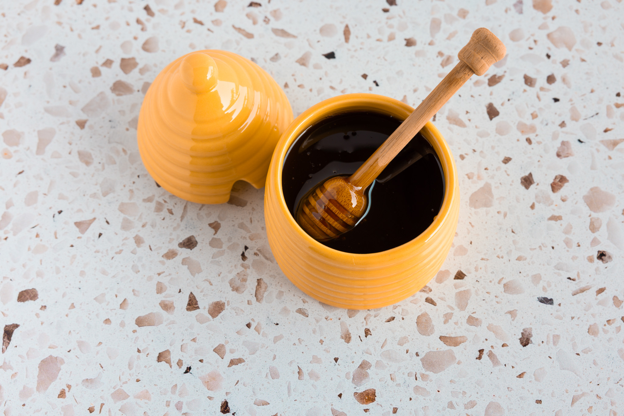Pote de mel amarelo de cerâmica com concha de madeira cheia de mel escuro
